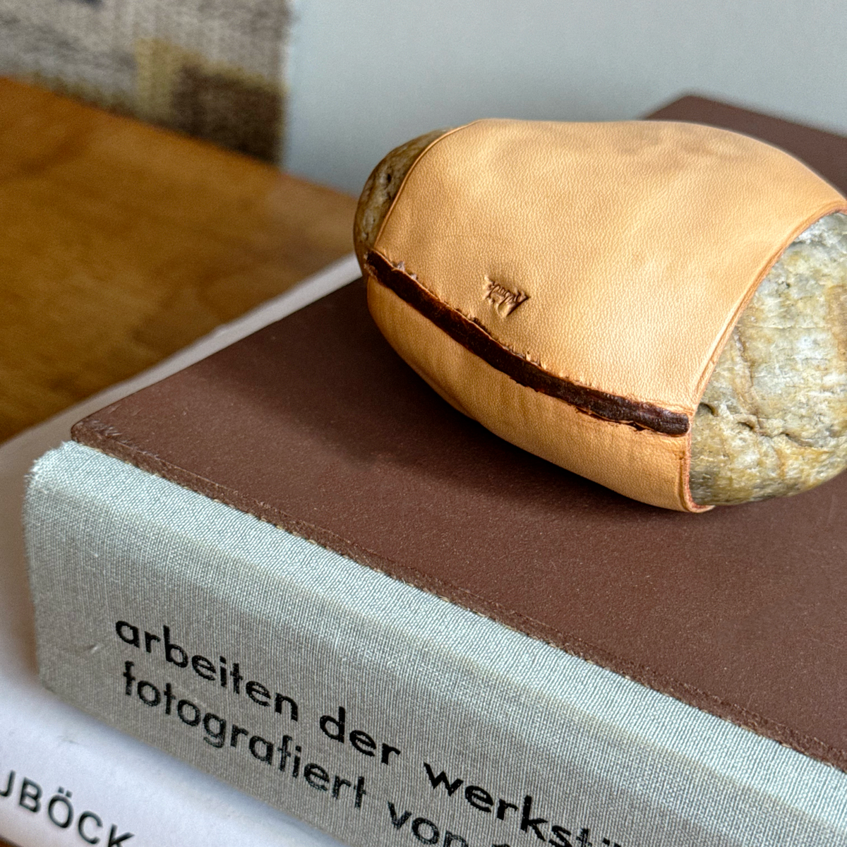 A handcrafted Austrian paperweight by Werkstätte Carl Auböck, featuring a smooth stone encased in rich leather. This sculptural mid-century design blends natural materials with refined craftsmanship, embodying Auböck’s distinctive modernist aesthetic.