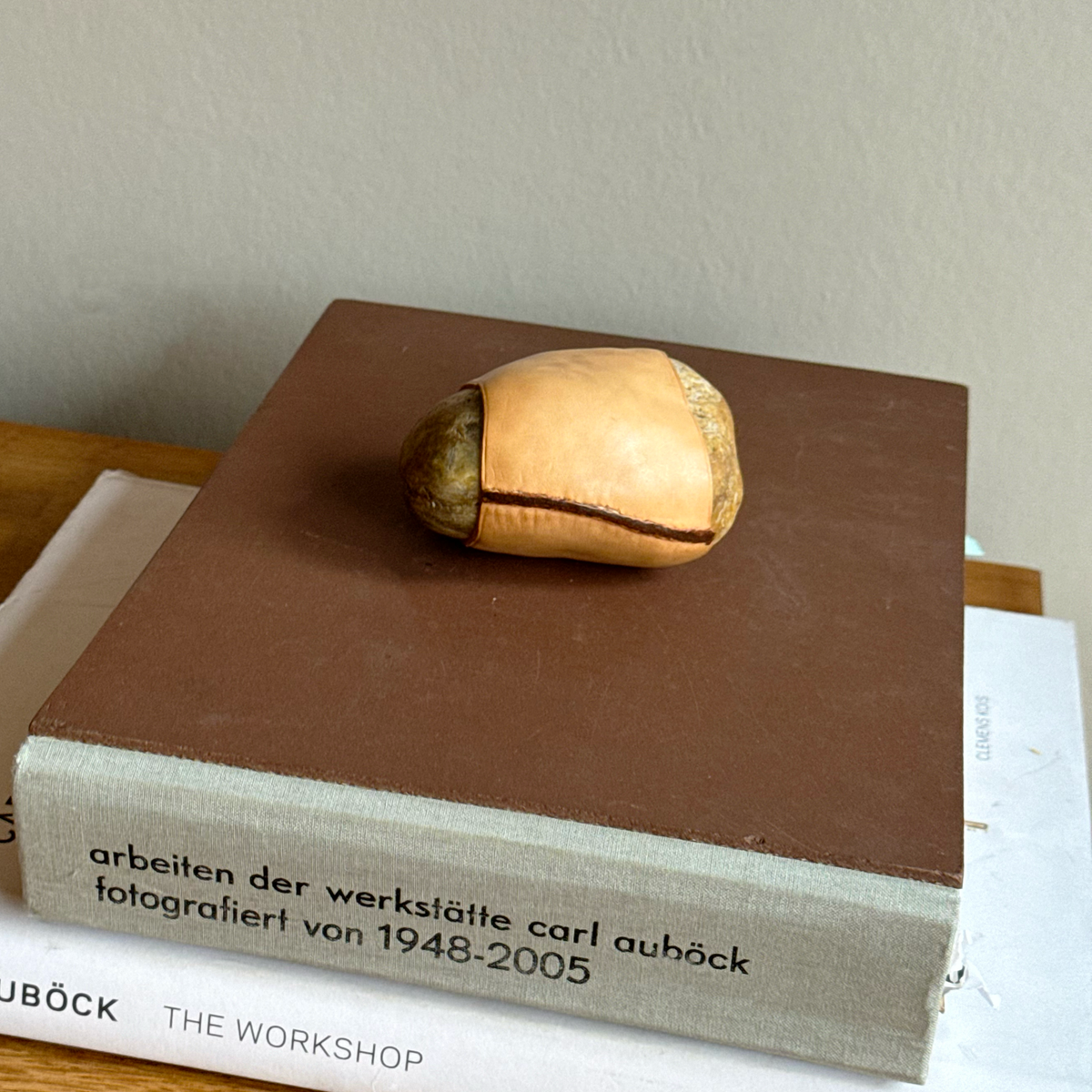 A handcrafted Austrian paperweight by Werkstätte Carl Auböck, featuring a smooth stone encased in rich leather. This sculptural mid-century design blends natural materials with refined craftsmanship, embodying Auböck’s distinctive modernist aesthetic.