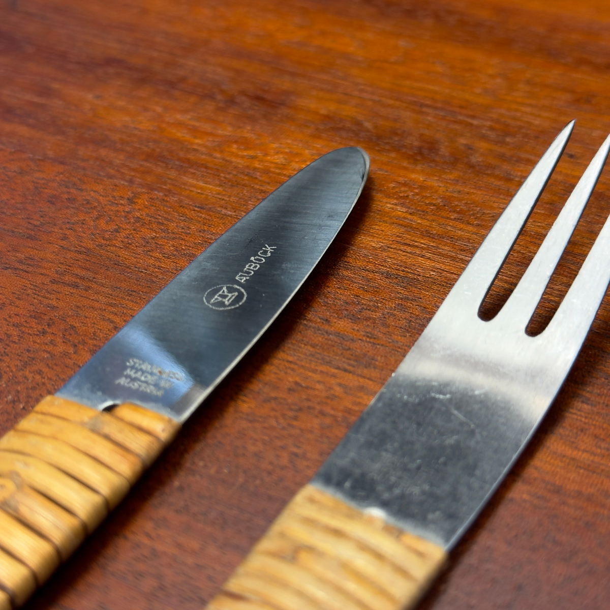 A vintage 1950s cutlery set by Carl Auböck, featuring a knife and fork with sleek steel blades and distinctive cane-wrapped handles. This mid-century design blends functionality with artisanal craftsmanship, showcased at Sigmar London.