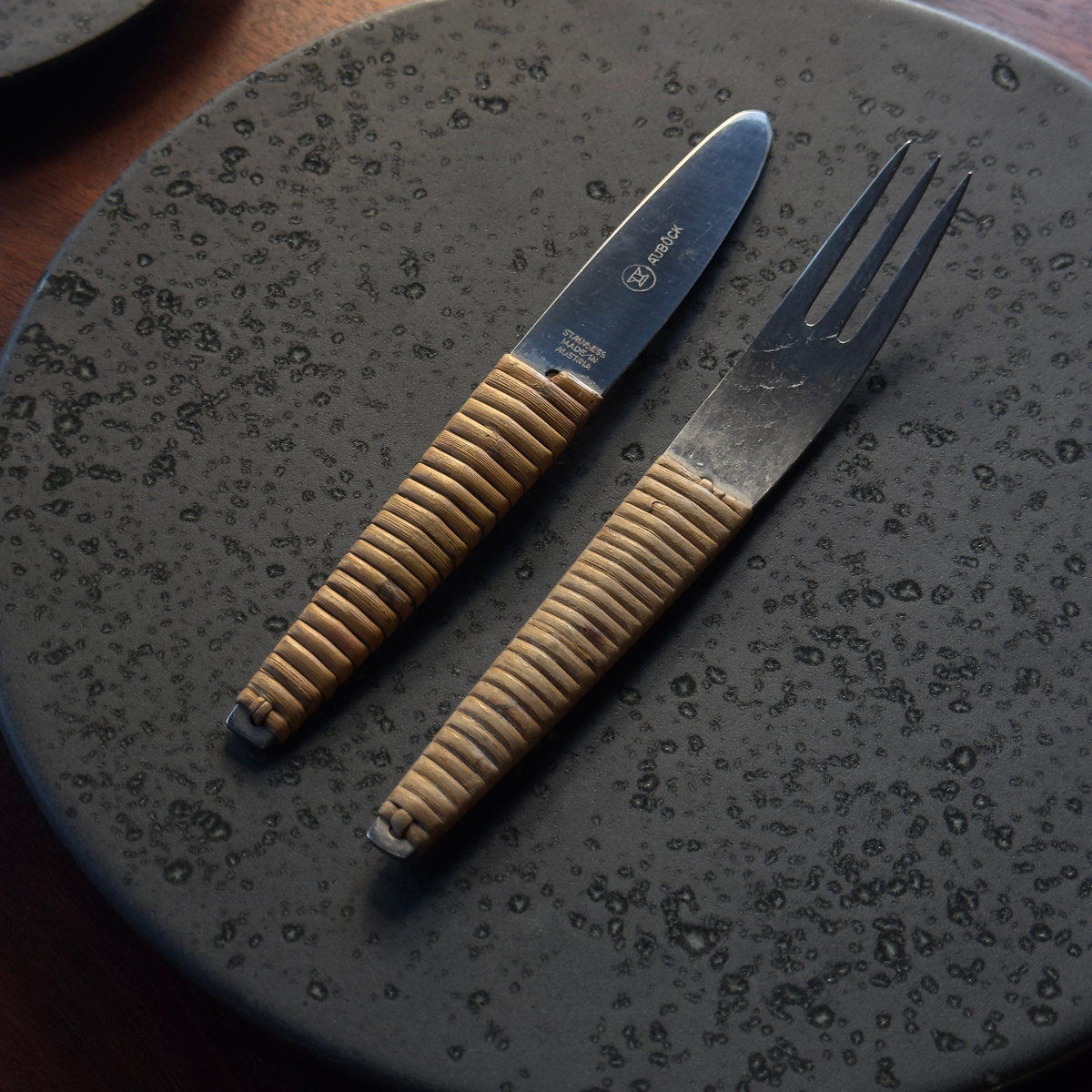 A vintage 1950s cutlery set by Carl Auböck, featuring a knife and fork with sleek steel blades and distinctive cane-wrapped handles. This mid-century design blends functionality with artisanal craftsmanship, showcased at Sigmar London.