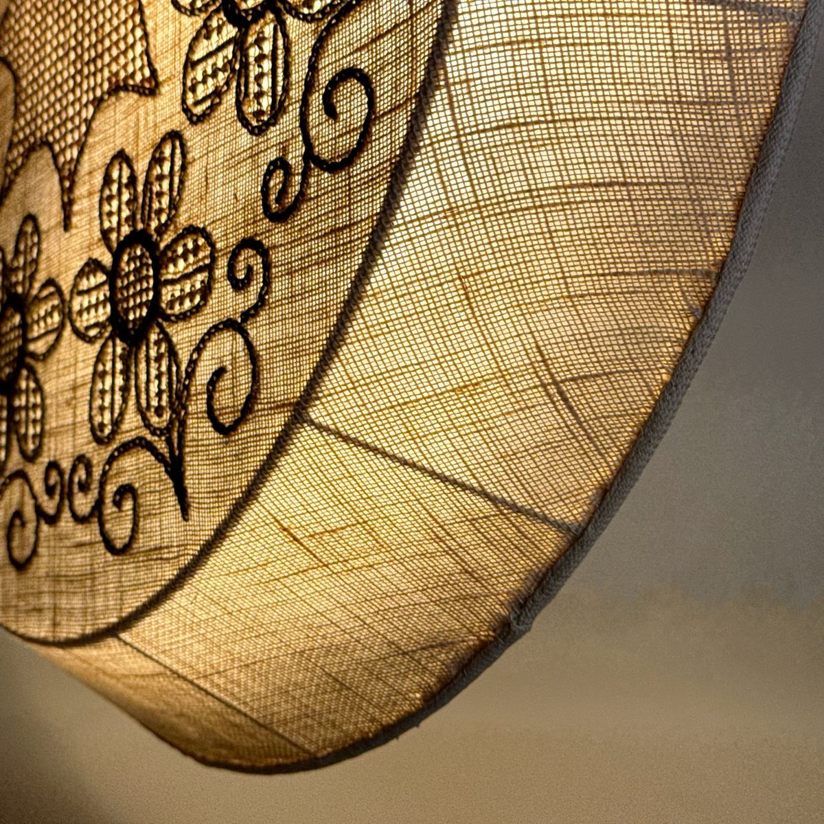 A unique lamp featuring intricate whitework embroidery, showcased at Sigmar London. Designed in the 1970s, the lamp emits a soft, diffused light through delicate stitched patterns, blending textile craftsmanship with functional lighting, from Sweden.