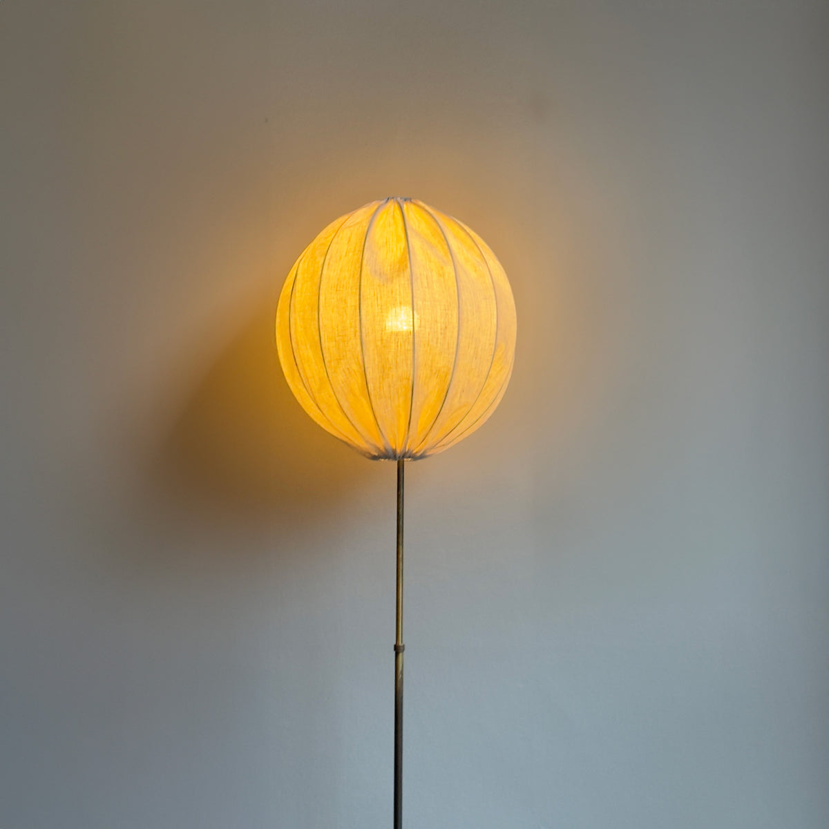 A vintage brass floor lamp with modern, spherical shade, finished in a light beige linen fabric. This lamp is available to purchase exclusively at Sigmar London. 