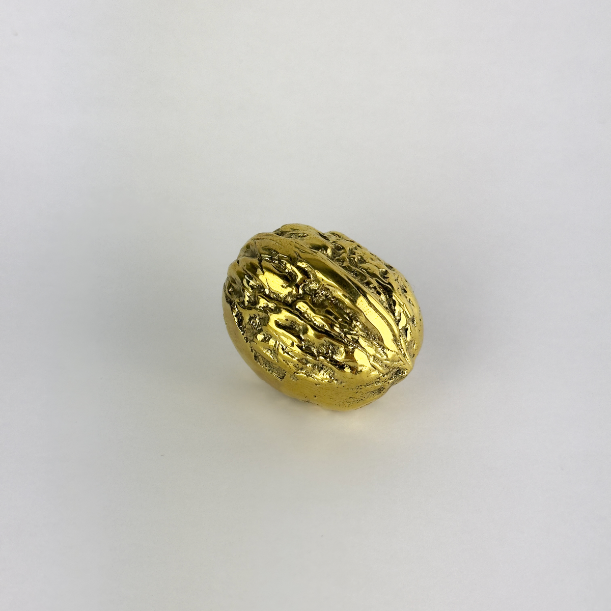 A walnut-shaped paperweight made of cast brass, created in Austria. This piece features modernist design with a blend of organic form and sleek craftsmanship.